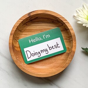 May include: A green name tag with the text "Hello, I'm Doing my best" in a wooden bowl.