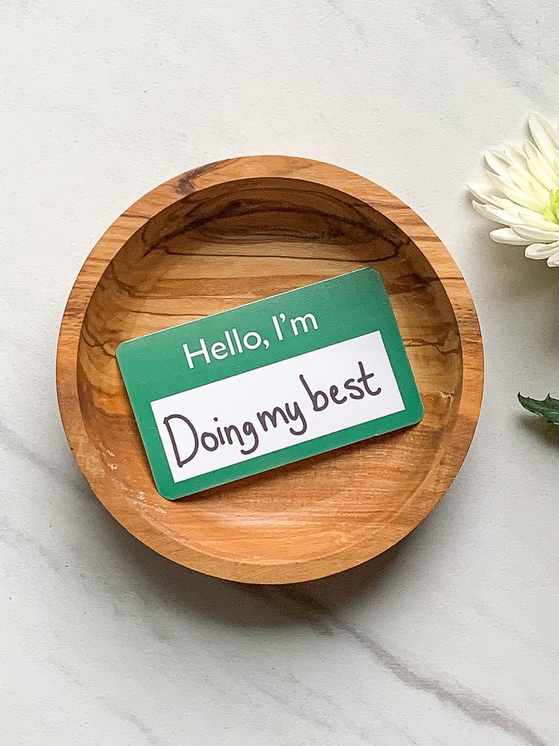 May include: A green name tag with the text "Hello, I'm Doing my best" in a wooden bowl.