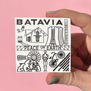 May include: A white square sticker with black line art illustrations and text. The word "BATAVIA" is at the top. Other images include a building, a bird, a bicycle, and the words "PEACE ON EARTH".