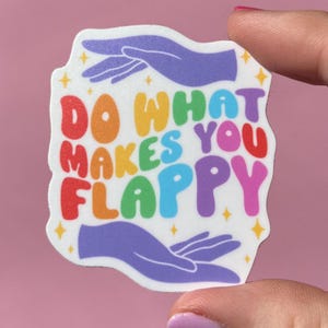 May include: A white sticker with a rainbow colored text that reads "Do what makes you flappy" with two purple hands on either side of the text.