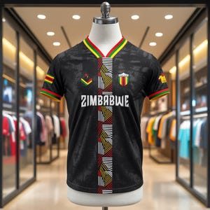 May include: Black soccer jersey with the word "ZIMBABWE" in white block letters. The jersey has a V-neck with green, yellow, and red trim. The sleeves also have the same trim. The jersey has a pattern of vertical stripes.