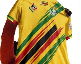 May include: A yellow short-sleeved t-shirt featuring diagonal brushstroke stripes in green, black, and red. The shirt displays the Zimbabwe flag, a soccer-themed crest, and a stylized emblem on the chest, with matching flag-colored sleeve cuffs.