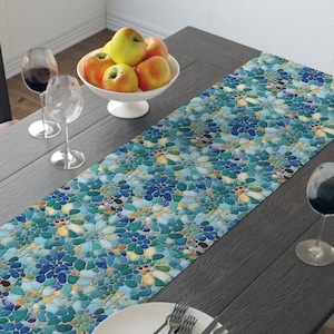 Peut inclure: Un chemin de table bleu et vert à motif mosaïque avec une assiette blanche et des couverts sur une table en bois foncé.