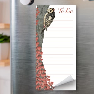 May include: A rectangular notepad with a woodpecker illustration, the words "To Do", and lined pages. The notepad features a tree trunk with red leaves and is attached to a silver refrigerator with magnets.