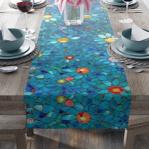 May include: A blue table runner with a mosaic pattern of colorful flowers. The runner is made of small, irregular pieces of glass that create a textured surface.