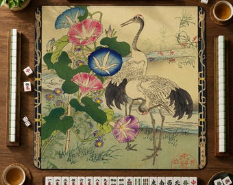 Pode incluir: Um tapete de mahjong quadrado com uma ilustração impressa de dois grous brancos com penas de asa pretas em pé perto de flores de glória-da-manhã cor-de-rosa e azuis. O tapete tem uma borda decorativa e é cercado por peças e chávenas.