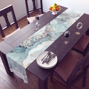 May include: A light blue and white table runner with a watercolor-like design. The runner is placed on a dark wood table with two chairs and wine glasses.