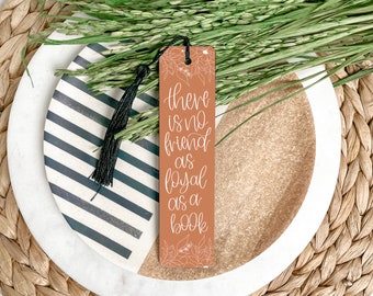 May include: A brown bookmark with a white tassel. The bookmark has white floral designs and the text "There is no friend as loyal as a book".