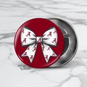 May include: A red and white button with a white bow with the letter "A" repeated on it. The bow is on a red background. The button is 2.25 inches in diameter.