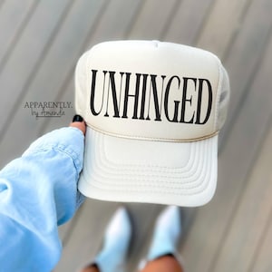 May include: A white trucker hat with a black mesh back. The hat has the word "UNHINGED" printed in black on the front.