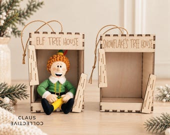 May include: Two light-coloured wooden tree house structures with twine hangers. One is engraved with ELF TREE HOUSE and contains a plush elf doll with orange hair, green shirt, and yellow trousers. The other is engraved with SNOWFLAKE'S TREE HOUSE.