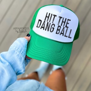 May include: Green and white trucker hat with the text "HIT THE DANG BALL" in black lettering.