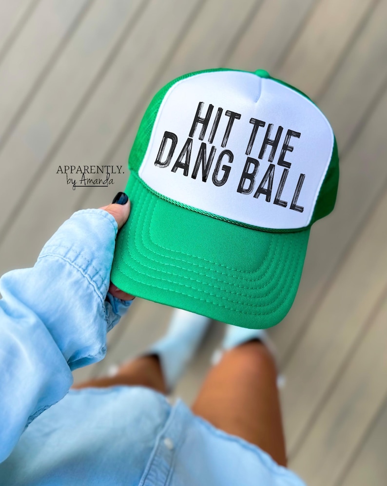 May include: Green and white trucker hat with the text "HIT THE DANG BALL" in black lettering.