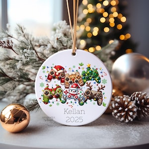 May include: White ceramic Christmas ornament featuring festive controller designs. The ornament includes a Santa controller, gingerbread controller, Christmas tree controller, snowman controller, and reindeer controller. The name "Kellan" and the year "2025" are printed on the ornament.
