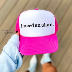 May include: A pink and white trucker hat with the text "i need an alani." in black lettering.