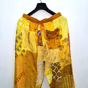Pode incluir: Calças largas com um design de patchwork em vários tons de amarelo, dourado e mostarda. As calças têm uma cintura elástica com cordão, dois bolsos frontais e uma silhueta de perna larga com punhos franzidos.