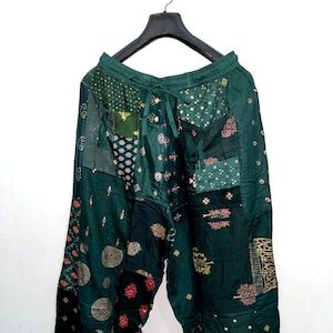 Könnte beinhalten: Dunkelgrüne Patchwork-Hose aus verschiedenen kontrastierenden Stoffbahnen mit unterschiedlichen Druckmustern in Gold, Rot und Weiß. Die Hose hat einen elastischen Bund mit Kordelzug und eine lockere, entspannte Passform.
