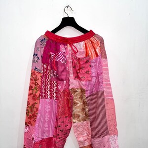 Pode incluir: Calças largas com um design de patchwork em vários tons de rosa, vermelho e laranja. A peça inclui uma cintura elástica com cordão, dois bolsos frontais e uma mistura de padrões florais, listrados e geométricos.