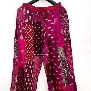 Pode incluir: Calças largas com design de patchwork em vários tons de magenta, bordô e roxo profundo. O tecido apresenta diversos padrões, incluindo motivos florais, grades geométricas e bolinhas. A cintura é elástica com um cordão de ajuste.