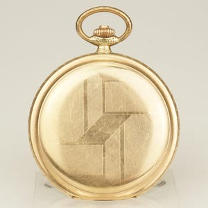 Puede incluir: Un reloj de bolsillo dorado con un diseño geométrico en la parte trasera. El reloj tiene una esfera circular con un patrón texturizado y un lazo en la parte superior para una cadena. Un artículo vintage.