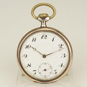 Puede incluir: Un reloj de bolsillo vintage con esfera blanca, números negros y un pequeño dial de segundos. El reloj tiene una caja dorada y una corona dorada. Las manecillas son oscuras. Un reloj clásico.