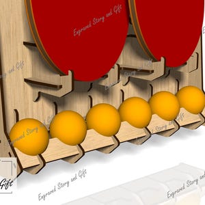 May include: Wooden ping pong ball and paddle holder. The holder is made of light-colored wood and features slots for balls and paddles. The paddles are red, and the balls are yellow. The text "Engraved Story and Gift" is visible.