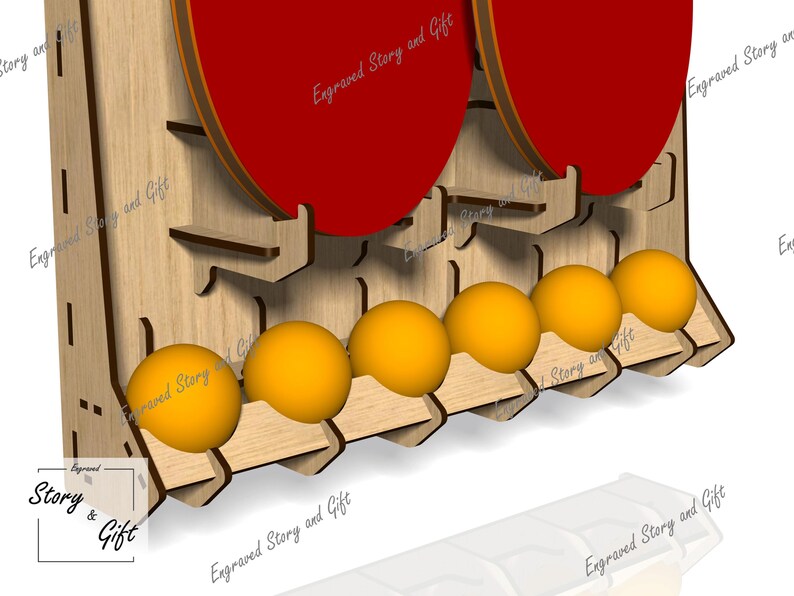 May include: Wooden ping pong ball and paddle holder. The holder is made of light-colored wood and features slots for balls and paddles. The paddles are red, and the balls are yellow. The text "Engraved Story and Gift" is visible.