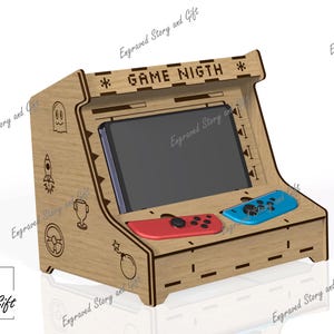 Puede incluir: Una consola de juegos de madera estilo arcade con el texto "GAME NIGHT" grabado en la parte superior. Cuenta con una ranura para una tableta o teléfono, y ranuras para mandos de juego rojos y azules. Los lados están decorados con gráficos grabados.