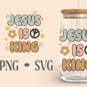 Op de afbeelding: Een glazen pot met een houten deksel en een rietje. De pot heeft een ontwerp erop dat "Jesus is Koning" zegt in een retro-lettertype met vredestekens en bloemen. Het ontwerp is in tinten groen, roze, oranje en zwart.