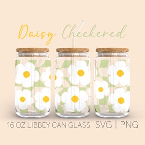 Op de afbeelding: Drie 16 ounce glazen blikbekers met houten deksels en heldere rietjes. De bekers zijn versierd met een wit madeliefjespatroon op een groen-wit geruite achtergrond. De tekst "Daisy Checkered" staat boven de bekers.