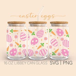 Op de afbeelding: Drie glazen potten van 473 ml met houten deksels en een rietje. De potten zijn versierd met een patroon van roze en witte paaseieren, groene bladeren en oranje wortels. De tekst "easter eggs" staat boven de potten.