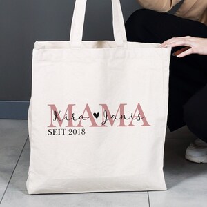 Może przedstawiać: Biała torba z płótna z różowym napisem "MAMA Kira Janis SEIT 2018". Między imionami znajduje się czarny symbol serca.