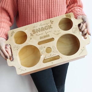 Könnte beinhalten: Ein Snacktablett aus Holz mit Fächern für Chips, Schokolade, Limonade und andere Snacks. Das Tablett ist mit dem Text "It's always snack time for Alina" graviert und hat auf einer Seite ein "yum!"-Etikett.
