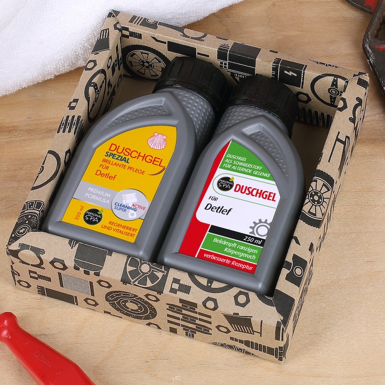 May include: Two grey bottles of Detlef brand shower gel in a brown cardboard box with a black and white pattern of car parts. The bottles are labelled "Duschgel Spezial" and "Duschgel".