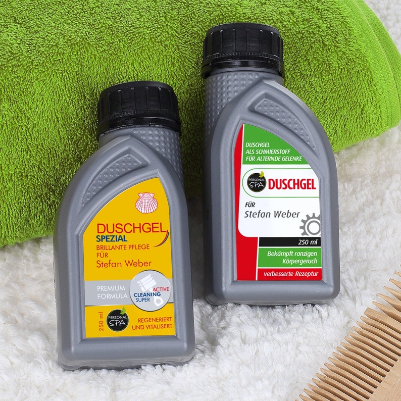 May include: Two grey bottles of shower gel with yellow and red labels. The labels say "Duschgel Spezial" and "Personal SPA Duschgel". The bottles are on a white fluffy surface with a wooden comb.