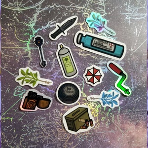 May include: A collection of stickers featuring various designs, including a knife, key, spray can, and a vial labeled "T-Virus." Other stickers depict a red and white umbrella logo, a film camera, and an ammunition box. The stickers are arranged on a map-like background.