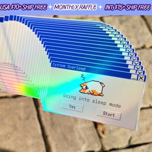 May include: A stack of iridescent stickers featuring a blue and white Windows 95 style error message that reads "System Overload" with a cartoon cat sleeping. The message below reads "Going into sleep mode" with two buttons that read "Yes" and "Start".