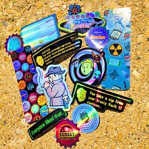 May include: A collection of colorful stickers with various designs and text. The stickers feature images of a cartoon character, a radiation symbol, and the text "Stay Classy New Vegas". Other stickers have the text "Everyone liked that."