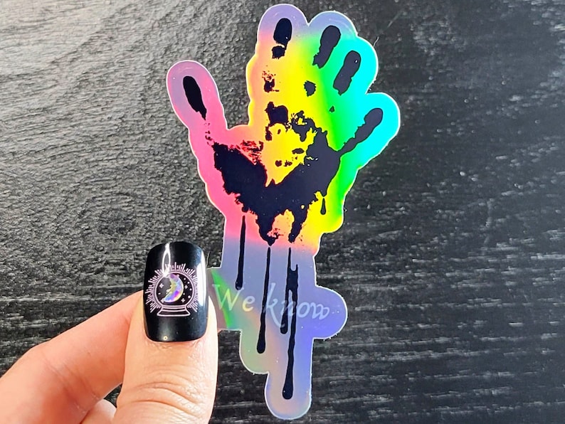 May include: A holographic sticker of a black handprint with dripping paint. The handprint is outlined in rainbow colors. The sticker has the text "We Know" at the bottom.