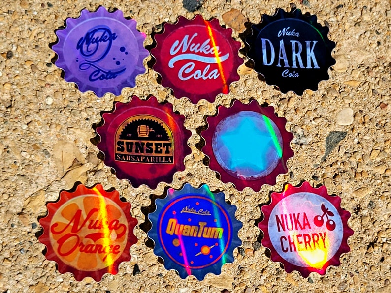 May include: A collection of eight bottle caps with various designs and text. The caps feature the words "Nuka Cola," "Sunset Sarsaparilla," "Nuka Dark," "Nuka Orange," "Nuka Quantum," and "Nuka Cherry." The caps have a metallic, iridescent finish.