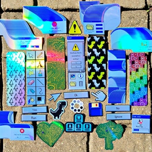 May include: A collection of colorful, retro-style stickers and bookmarks. Designs include computer interface elements, dinosaur graphics, and text prompts like "Yes," "No," and "Run." The items are arranged on a textured surface.