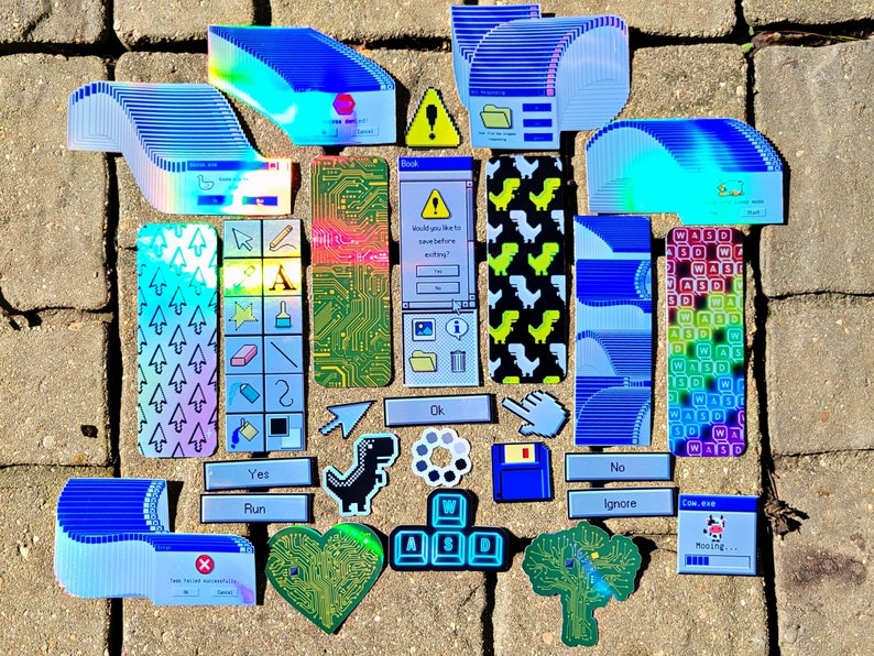 May include: A collection of colorful, retro-style stickers and bookmarks. Designs include computer interface elements, dinosaur graphics, and text prompts like "Yes," "No," and "Run." The items are arranged on a textured surface.