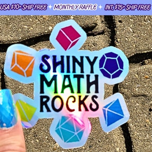 May include: Holographic sticker with the text "SHINY MATH ROCKS" surrounded by colorful geometric shapes. The sticker has a rainbow sheen and is held up by a hand with iridescent nail polish.