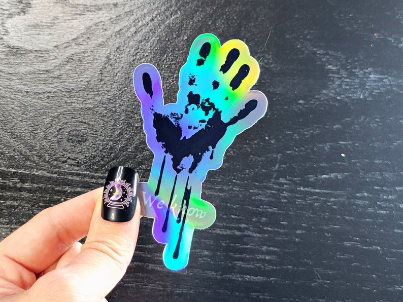 May include: A holographic sticker of a black handprint with dripping paint. The sticker has a rainbow iridescent finish.