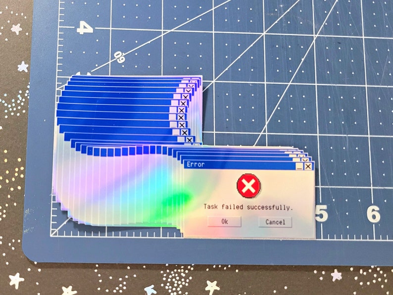May include: A holographic sticker with a blue and white color scheme. The sticker is a parody of a Windows error message. The text on the sticker reads "Error: Task failed successfully. Ok Cancel".