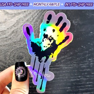 May include: A holographic sticker of a black handprint with dripping paint. The sticker has a rainbow iridescent finish.