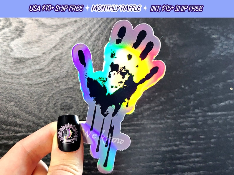 May include: A holographic sticker of a black handprint with dripping paint. The sticker has a rainbow iridescent finish.