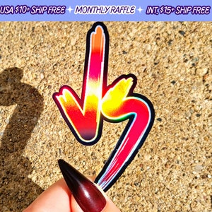 May include: A colourful sticker with a red, orange, yellow and blue gradient design. The sticker is shaped like a downward arrow and a curved line. The sticker is on a brown, textured surface.