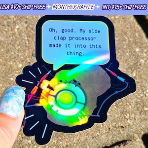 May include: A holographic sticker with a black background featuring a green, yellow, and red image of a portal gun from the video game Portal. The sticker has a speech bubble with the text "Oh, good. My slow clap processor made it into this thing."