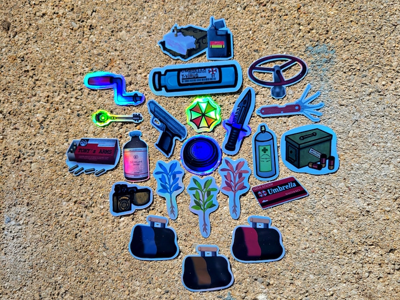 May include: A collection of holographic stickers featuring various designs. Includes a key, a gun, a knife, a steering wheel, a vial labeled "T-VIRUS", a box of ammunition, and a red and black bag. The stickers are on a textured, light brown surface.